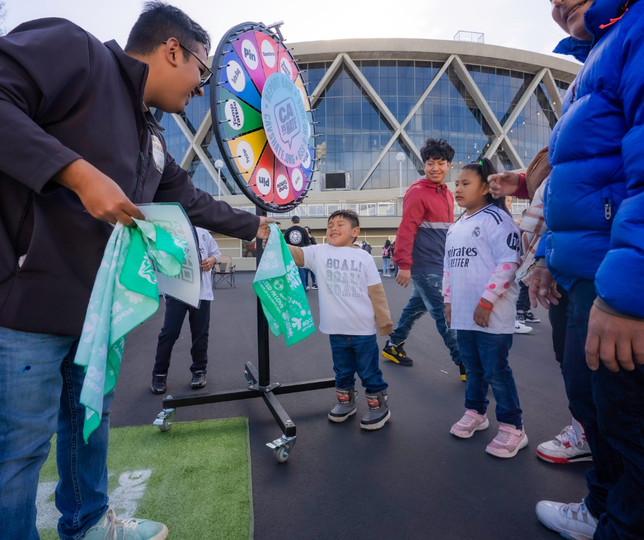 Staff hand out bandanas to children at a California Versus Hate table during an Oakland Roots game.