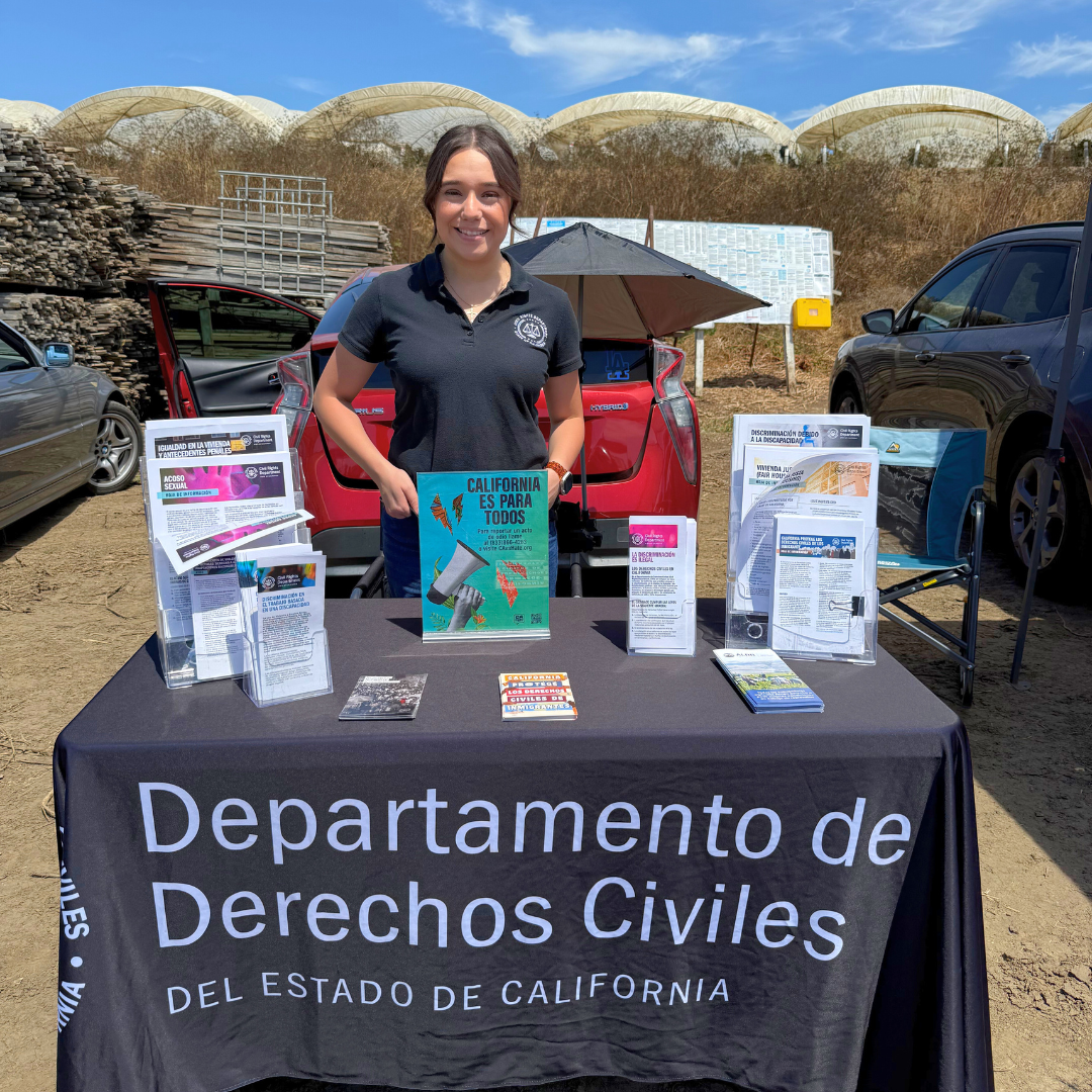 Lupe smiles while standing at a resource table for farmworkers at a worksite in California.