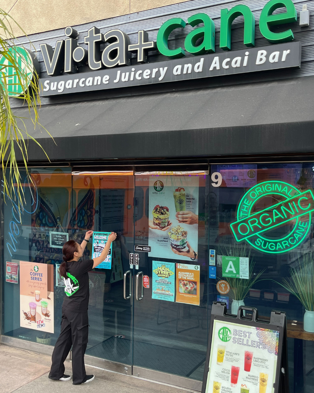 Allison the owner of Vita Cane juicery and acai bar in Alhambra hangs up a sign for the Welcome In program outside the business.