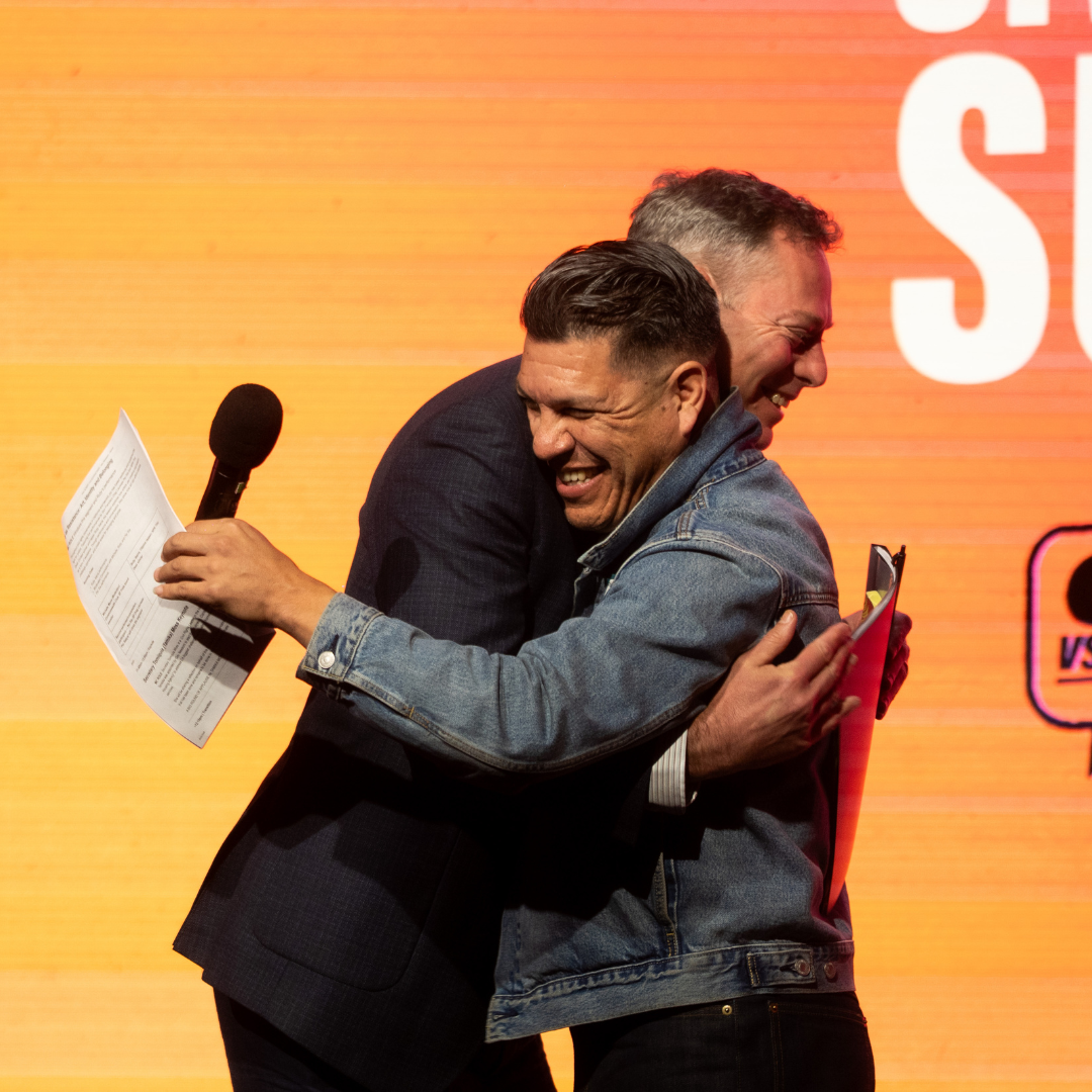 Musician and activist  Hector Flores hugs California Civil Rights Department Director Kevin Kish on stage during the California Civil Rights Summit.
