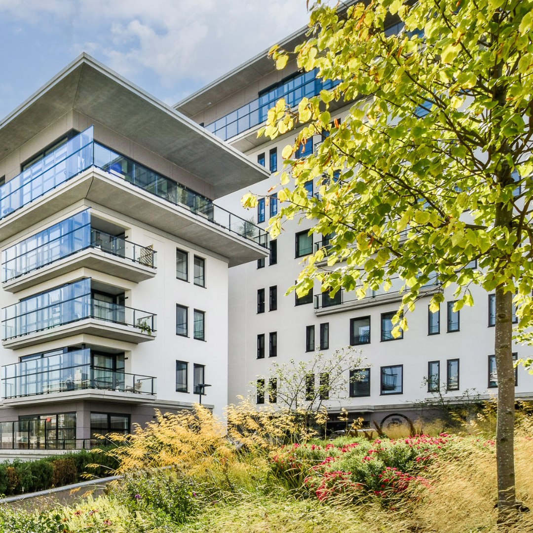 A white modern apartment complex with trees and landscaping.