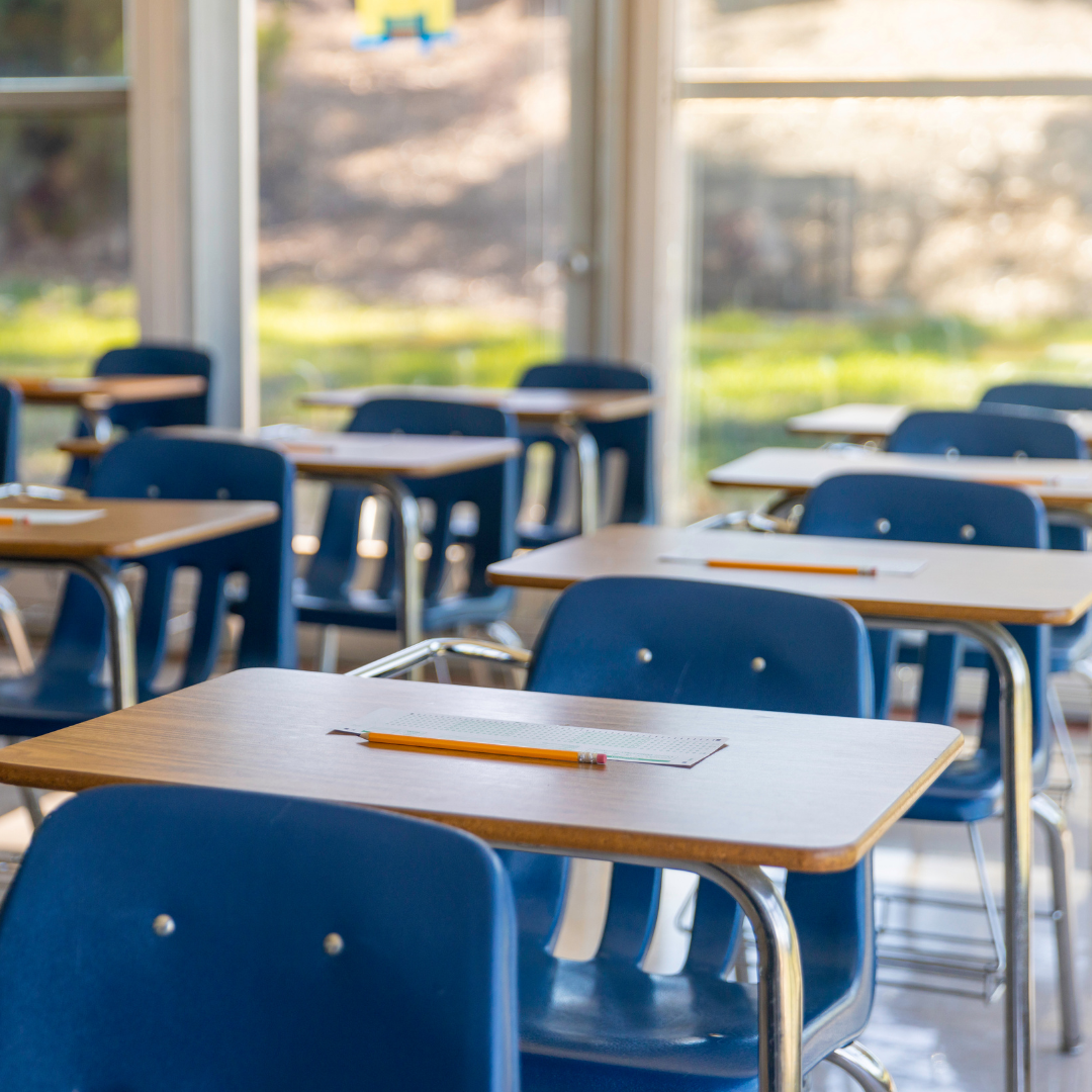 A row of blue chairs and wooden desktops inside a classroom. 