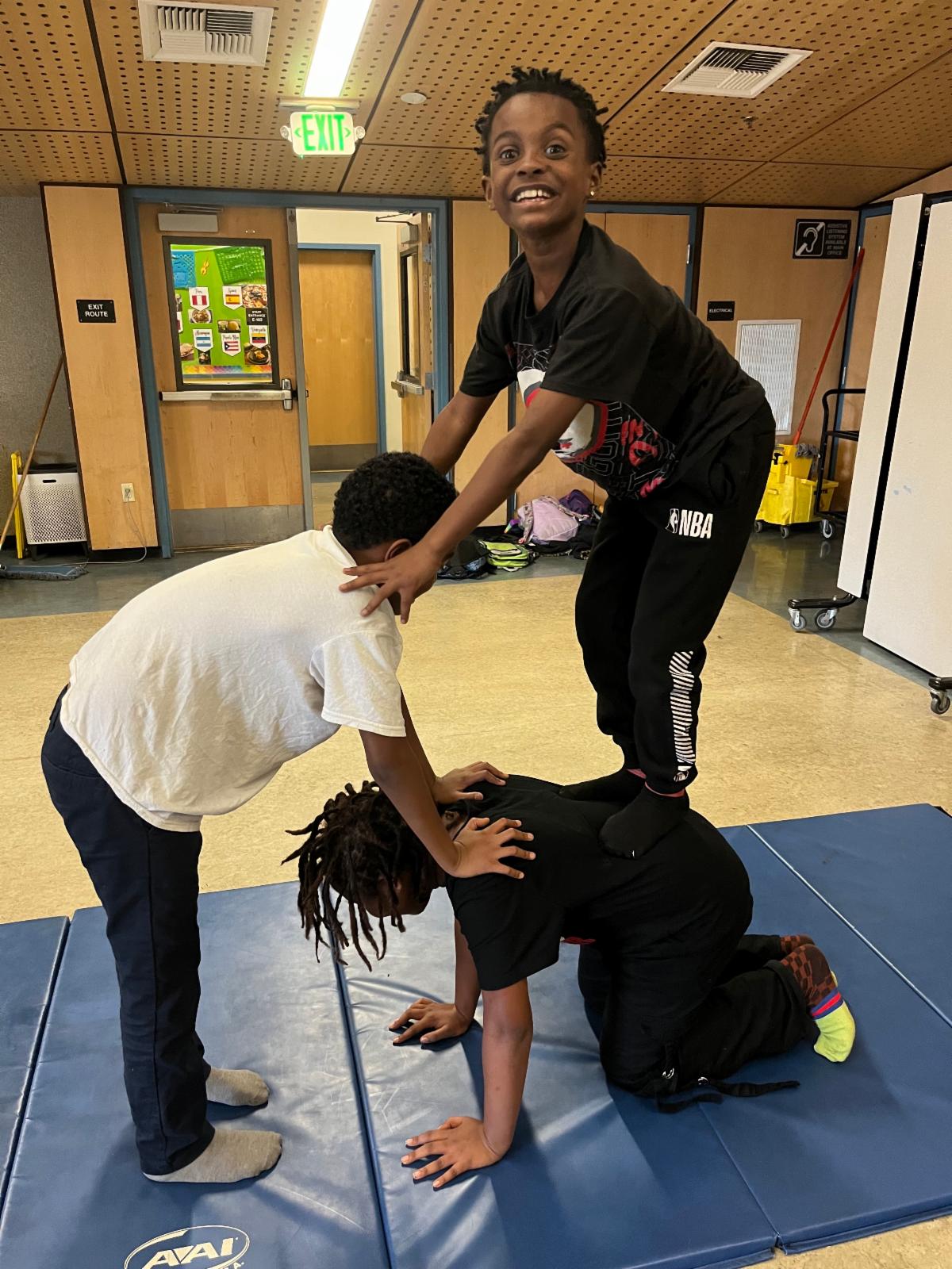 Three students create a human pyramid with the top stander looking at the camera with a big smile