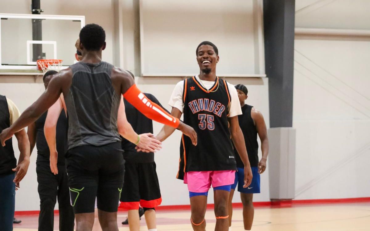 Man reaches arm out to high-five two teammates as he smiles and walks off basketball court.