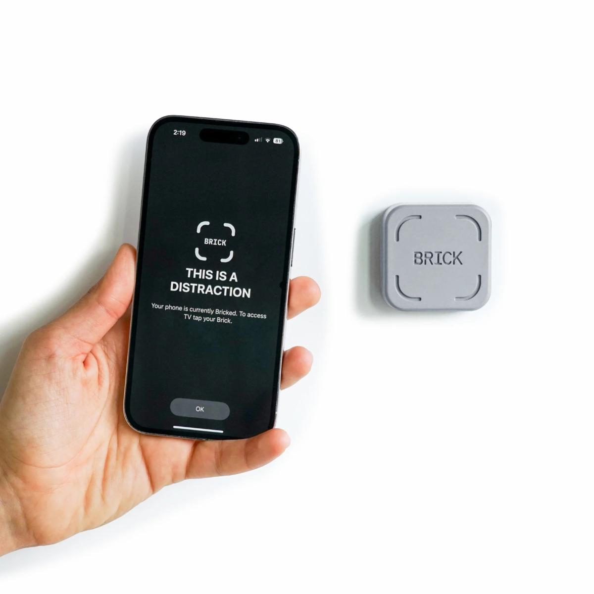 Someone holding a phone that says brcik a distraction with the brick sitting next to the phone