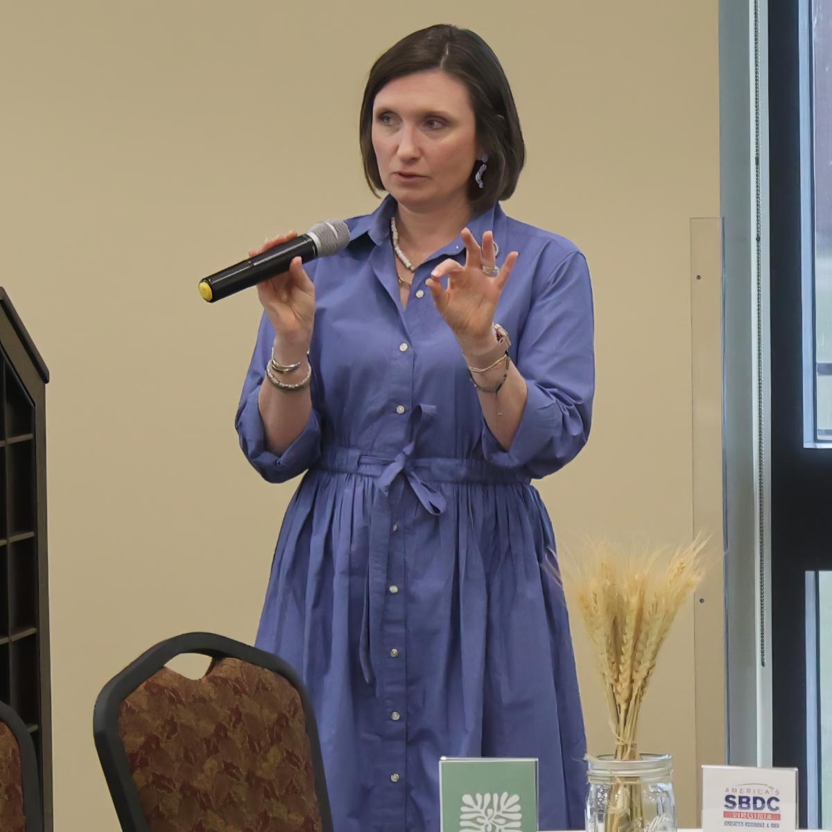 A woman in a blue dress holding a microphone with a chair and table decorations in front of her