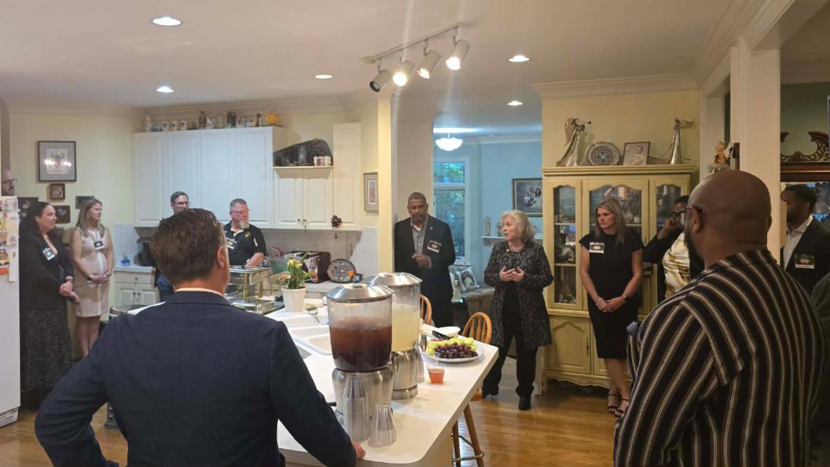 A group of Ferrum College alumni, staff. and faculty gathered in a kitchen listening to President Martin