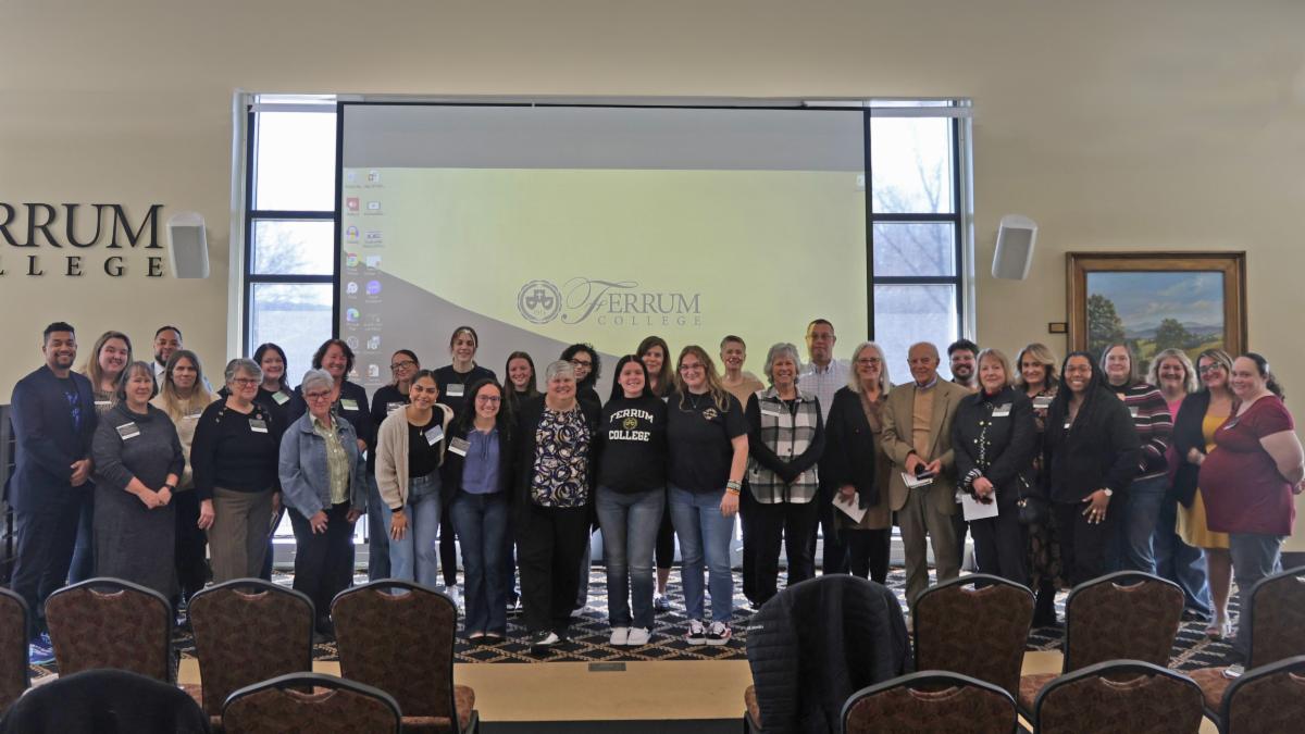 A large group of Ferrum College alumni, faculty, and staff posing for a group photo in front of a screen