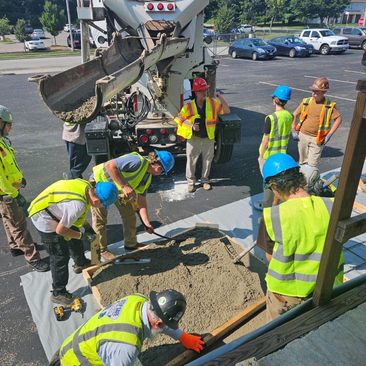 Construction workers in safety gear pouring concrete at a job site, collaborating on a project with machinery in the background.
