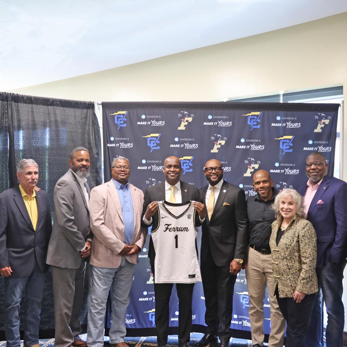 Group of people celebrating a new basketball coach at a press conference, showcasing teamwork and community spirit.