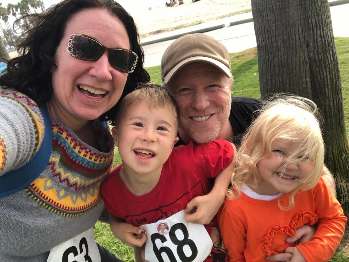 Kelly Rain and family at a park wearing numbered bibs from a walk-a-thon and smiling