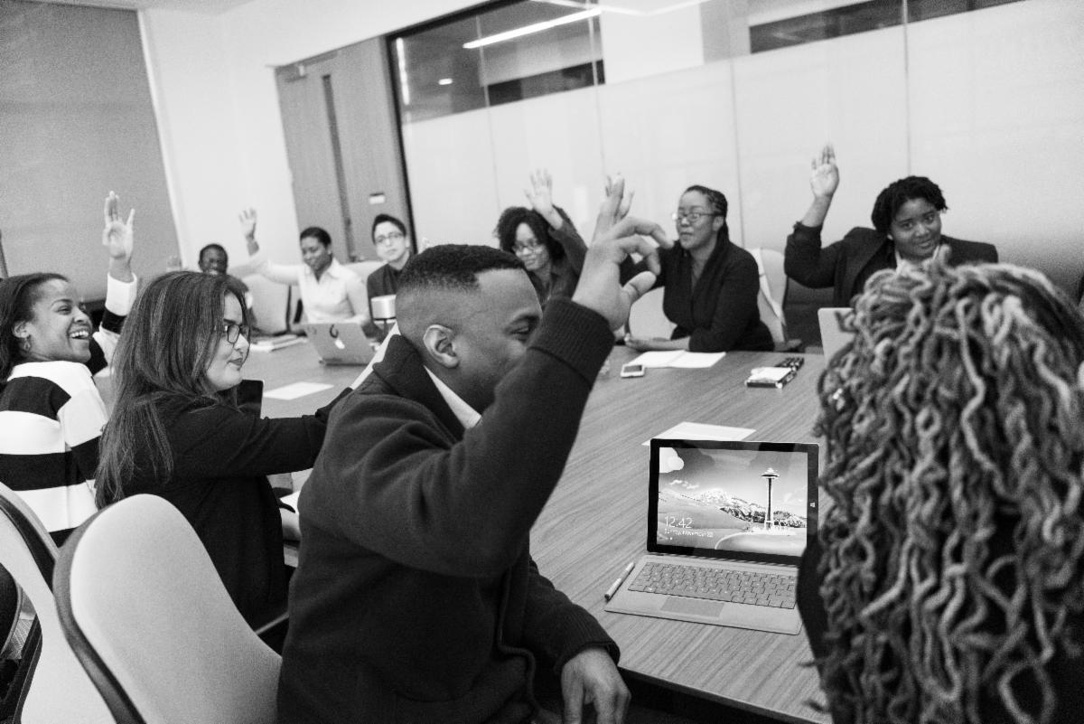 adults raising hands seated at conference table