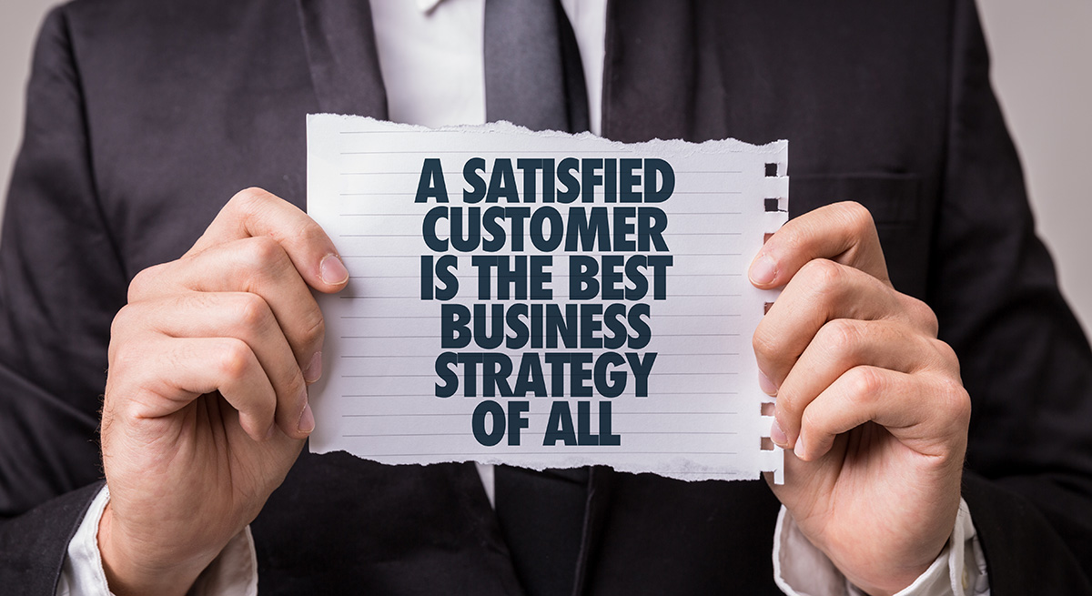 photo of a man holding a piece of paper that says A SATISFIED CUSTOMER IS THE BEST BUSINESS STRATEGY OF ALL