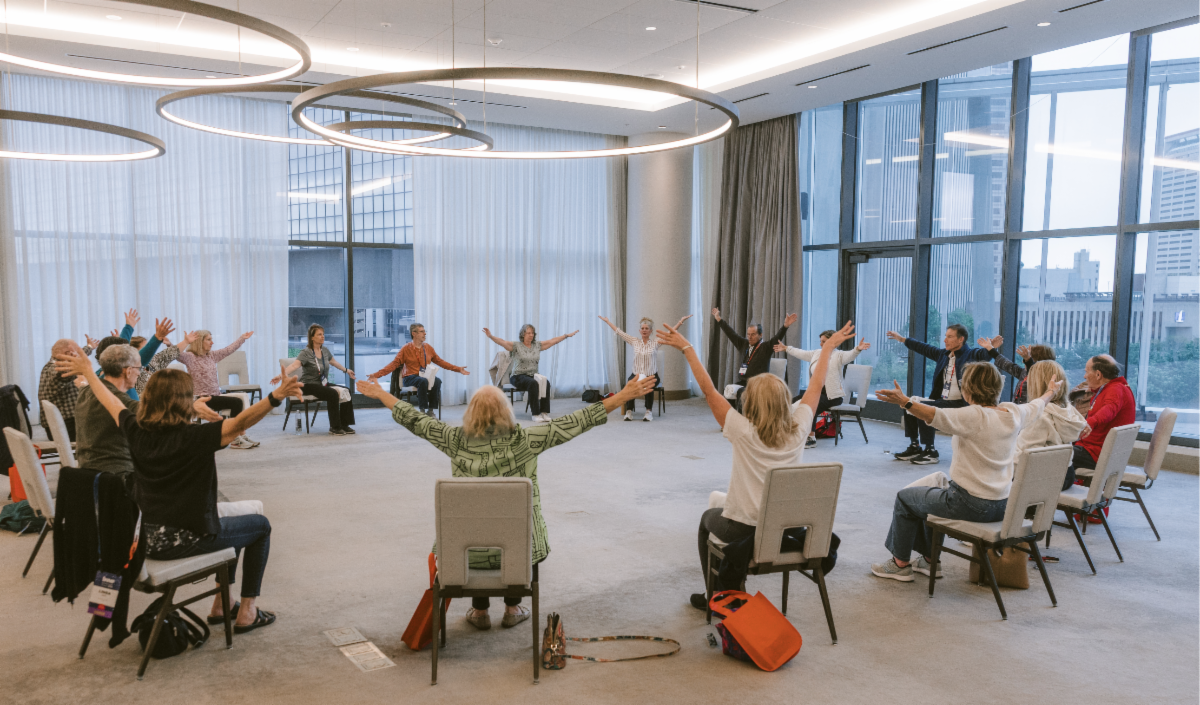 Circle of WM patients and caregivers seated with arms lifted during wellness session