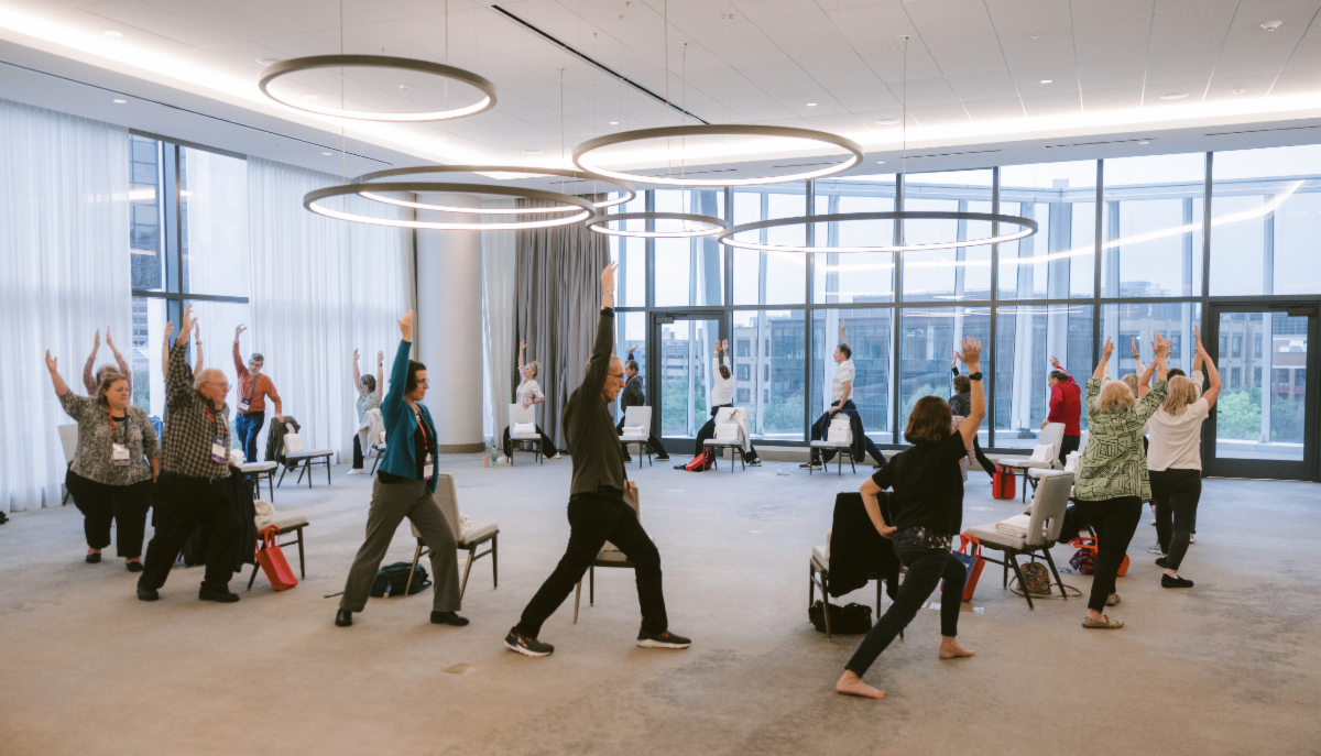 Circle of WM patients and caregivers standing in warrior one pose during wellness session