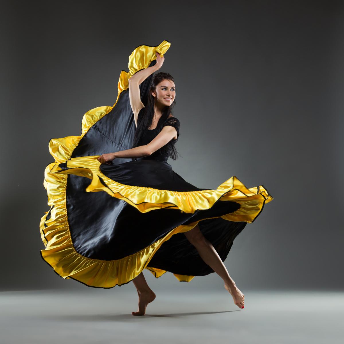 Smiling woman in black and yellow dress is dancing. Full length studio shot on gray background.