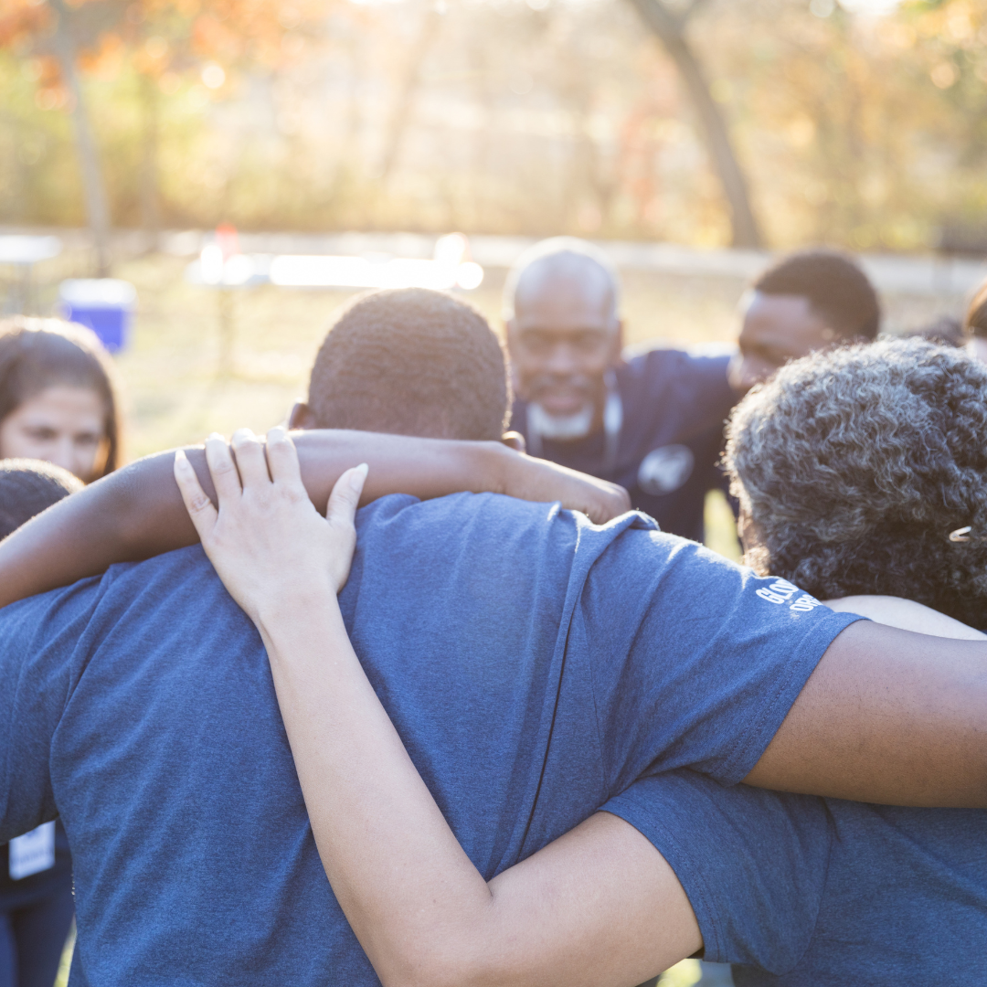 People standing in a circle with their arms around each other 