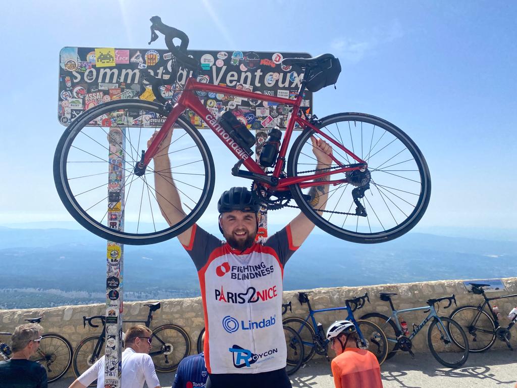 A photograph of Mark Renaghan in his cycling gear, holding his bike above his head.