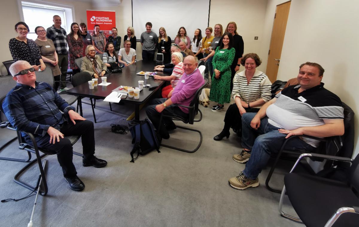 A photograph of a large group of people in the office of Fighting Blindness. There is a Fighting Blindness banner in the background.