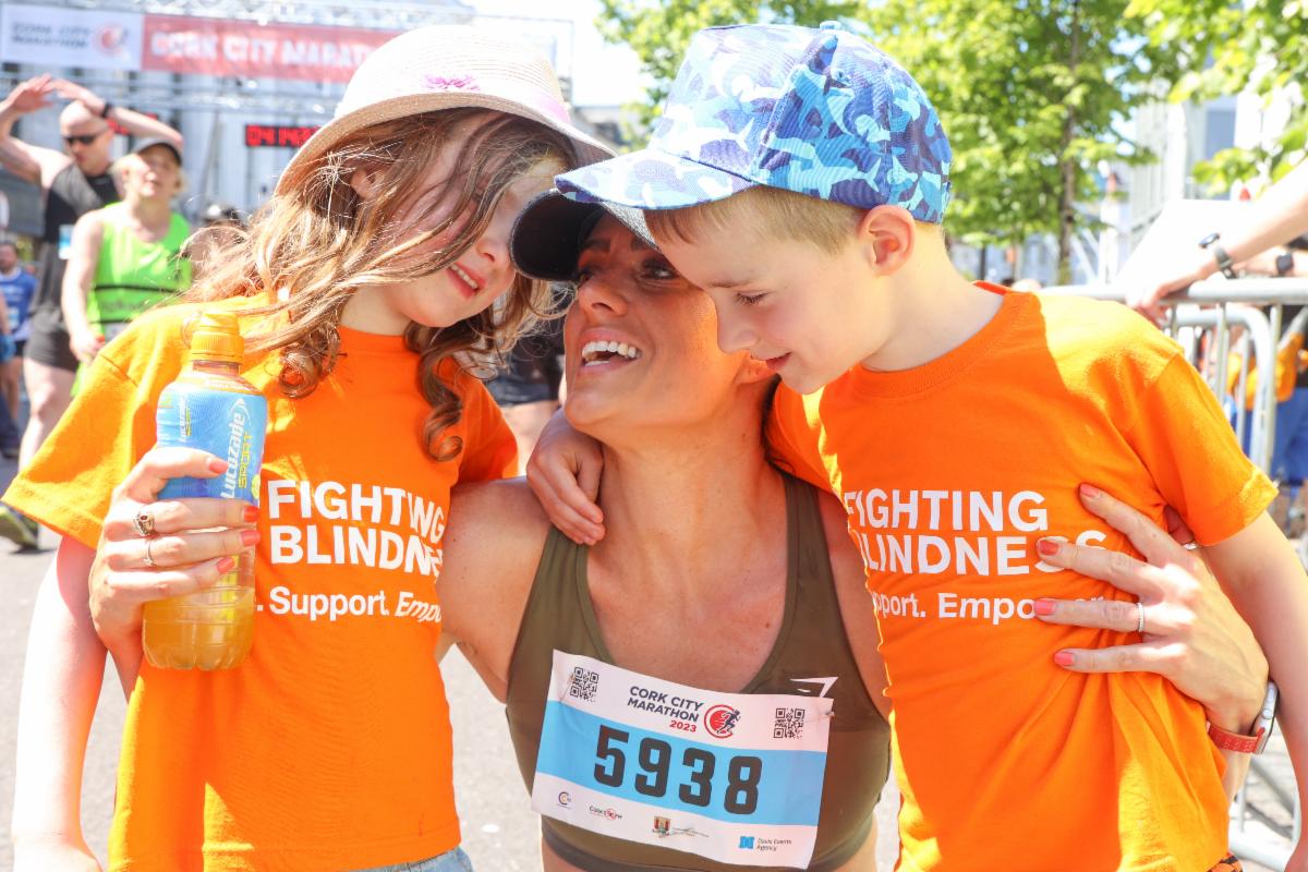 Photograph of Lisa Delaney, with her children Cathal and Caragh Sheehan, after crossing the finish line at the Cork City Marathon on Sunday, June 4. They are all smiling. Lisa is wearing a marathon race number. Both children are wearing Fighting Blindness orange t-shirts with the charity logo clearly visible.