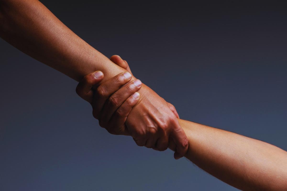 image of two arms and hands reaching across clasping hands