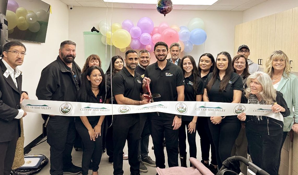 16 people inside the newly opened Kids Dental Pals right before cutting the grand opening ribbon