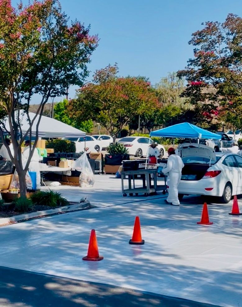 Household Hazardous Waste drop off parking lot with white plastic on ground and orange cones with shite car and workers in white jumpsuits carrying waste from car trunk