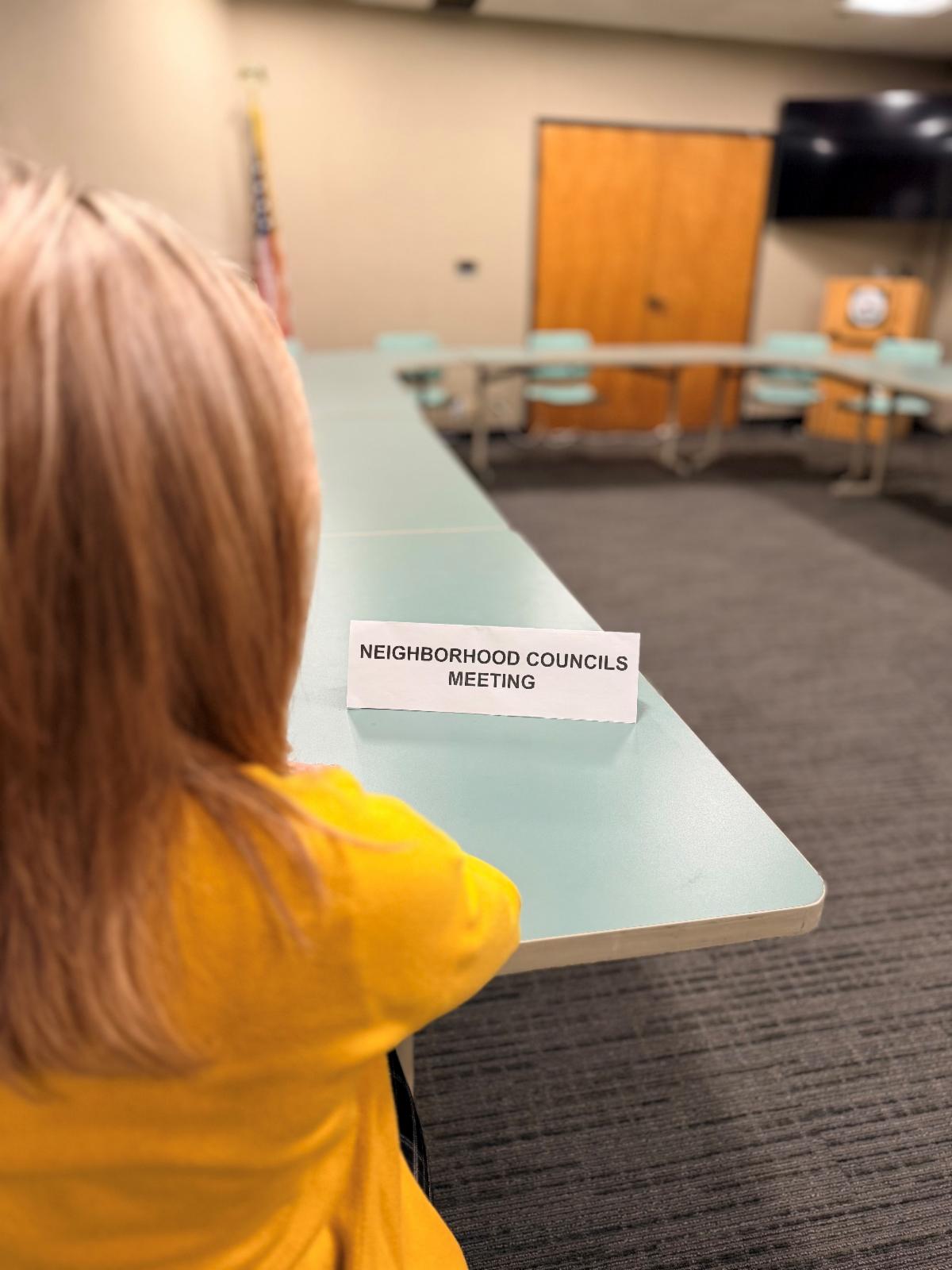 woman seated with a Neighborhood Council meeting table tent in front of her