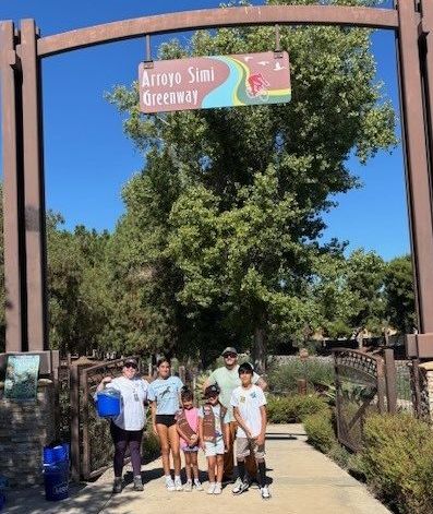 Two adults and four kids ready to volunteer for Coastal Cleanup Day standing under Arroyo Simi sign