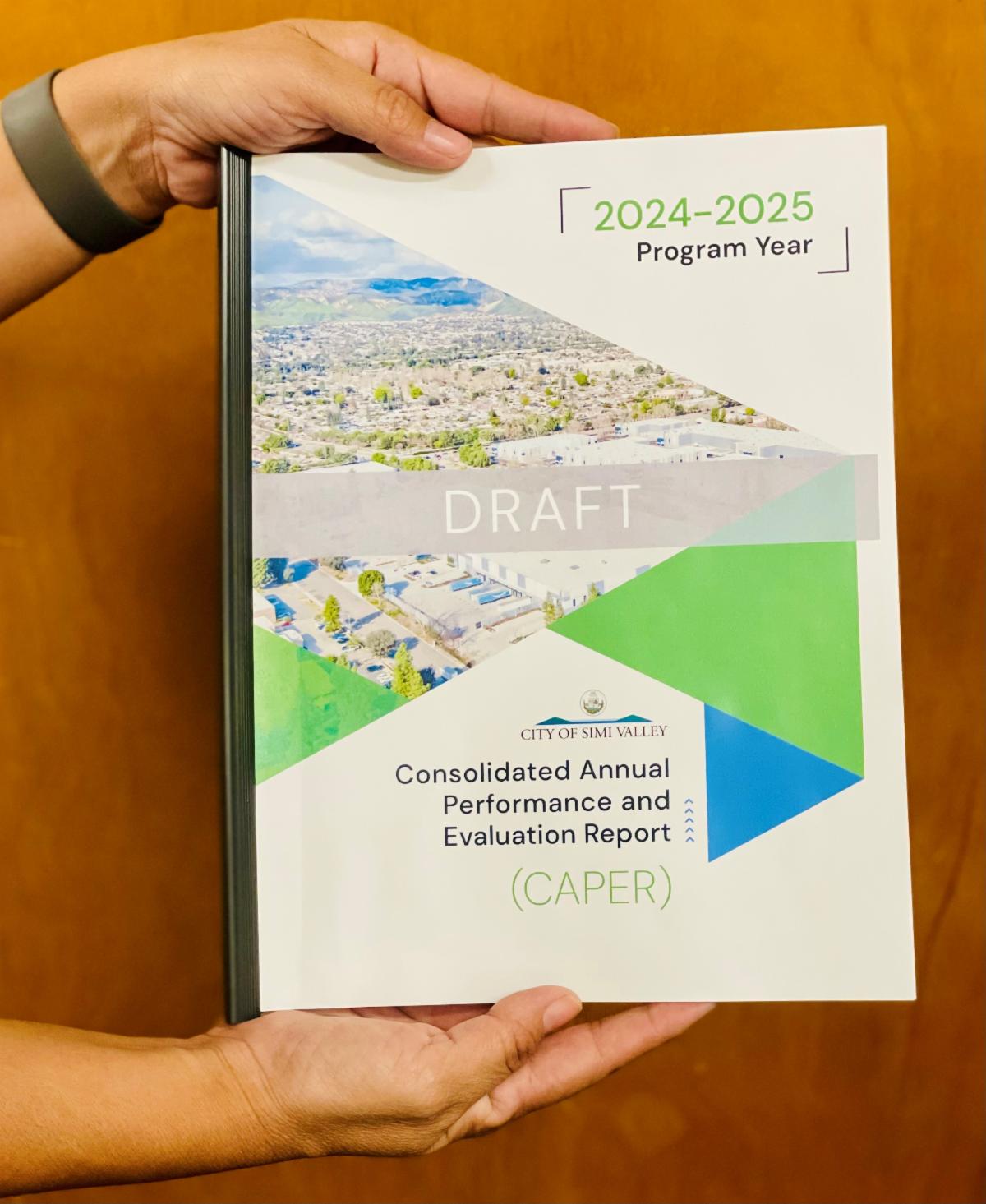 Staff member holding the Draft Fiscal Year 2024-25 Consolidated Annual Performance and Evaluation Report document