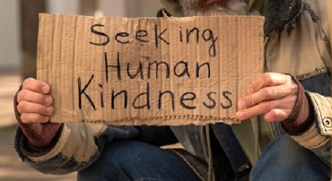 Unhoused individual holding a Seeking Human Kindness sign
