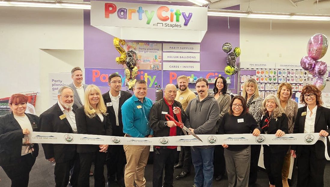 Large group cutting a ribbon in front of newly opened Party City section in Staples