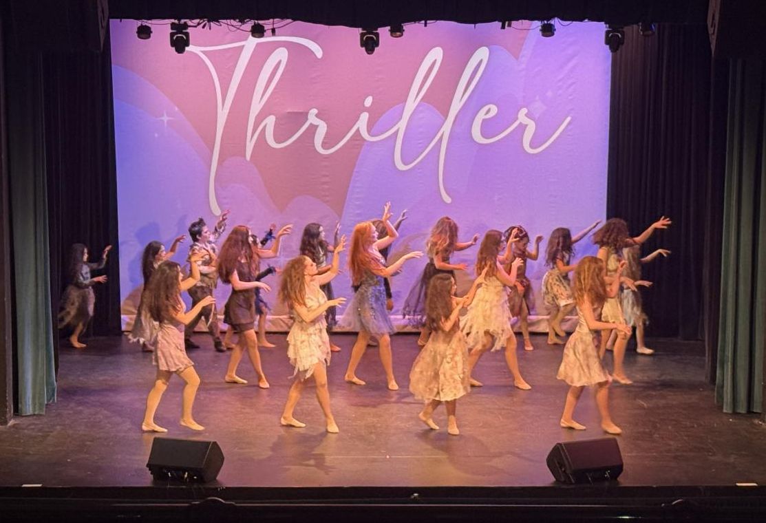 twelve female students wearing pale neutral-colored knee length dresses dancing on stage