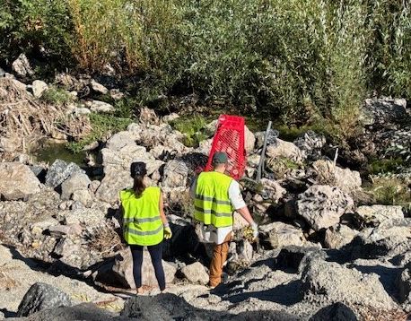 a woman and man wearing yellow volunteer vests hiking down to remove a grocery cart from the Arroyo Simi