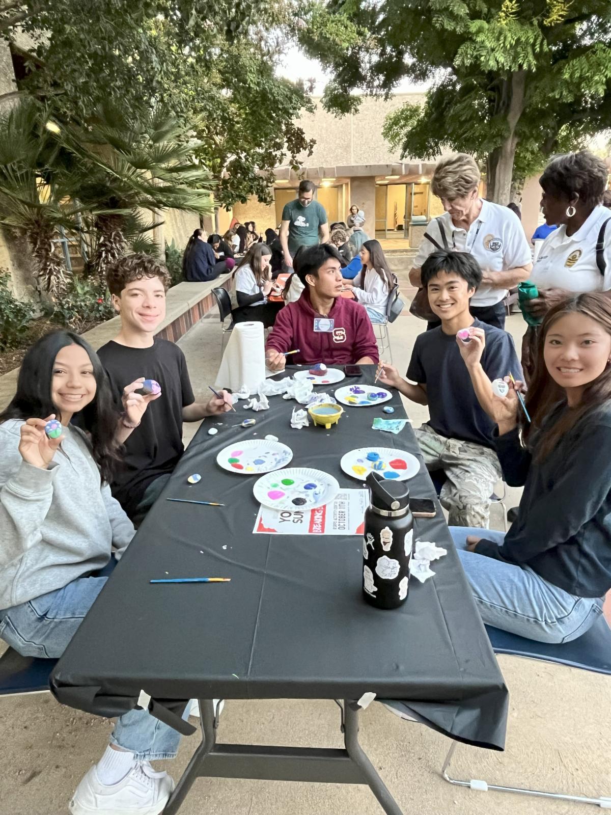 Group of students sitting at a table displaying their painted rocks.