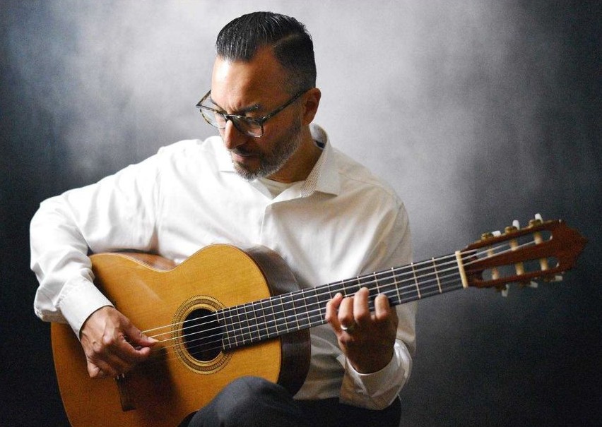 Man with glasses playing an acoustic guitar