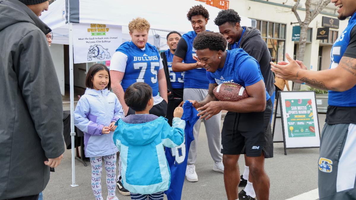 College of San Mateo football players greet young fans on B Street