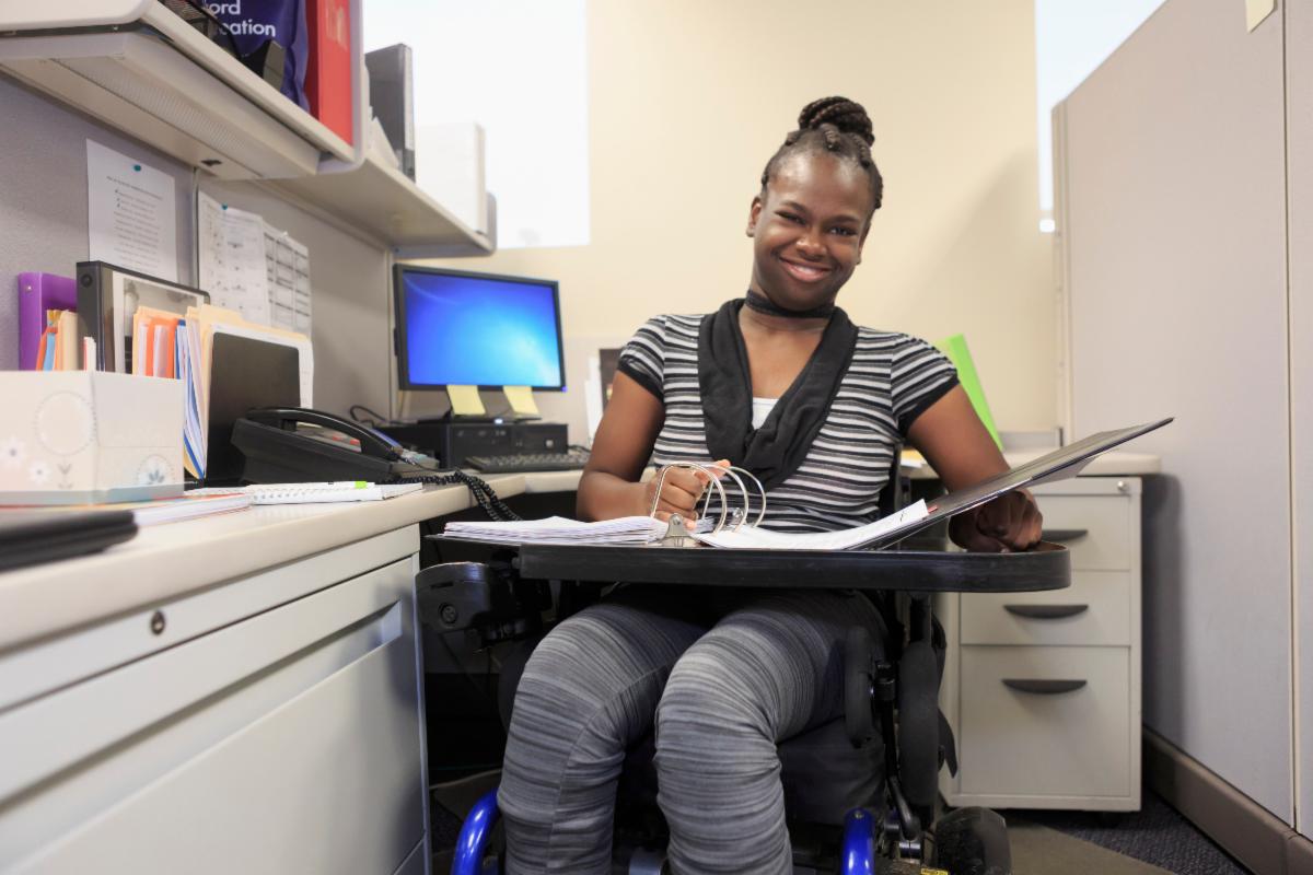 Person using wheelchair holding binder and working in an office
