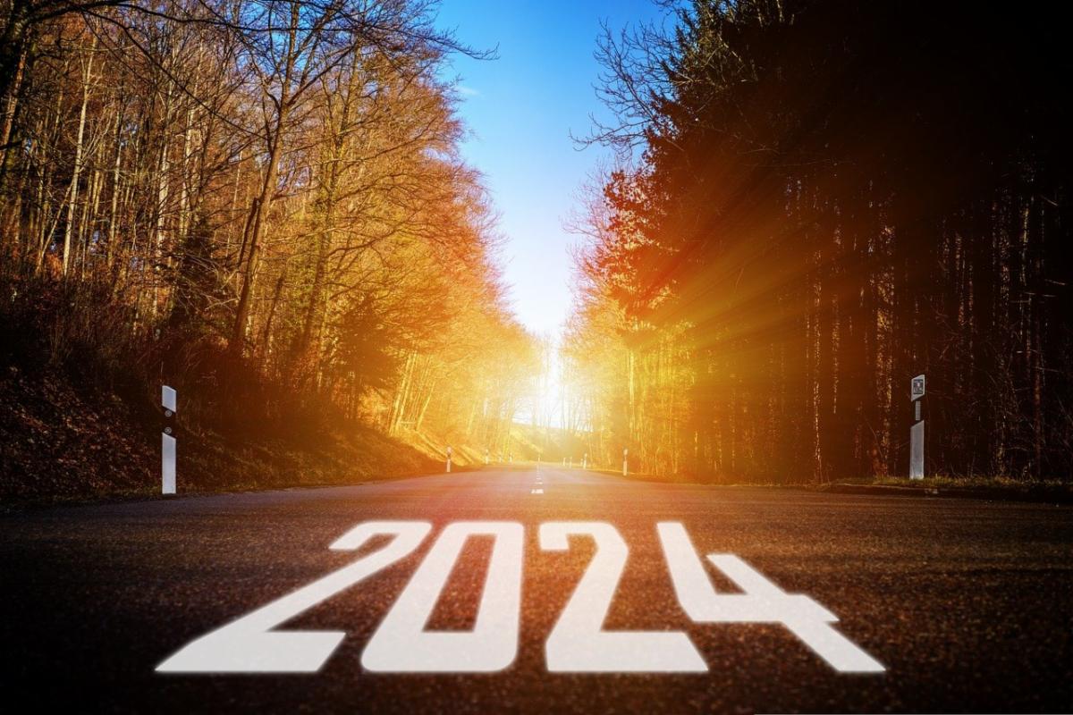 2024 written out in white on a road the sign is rising on the horizon between two lines of trees on each side of the road