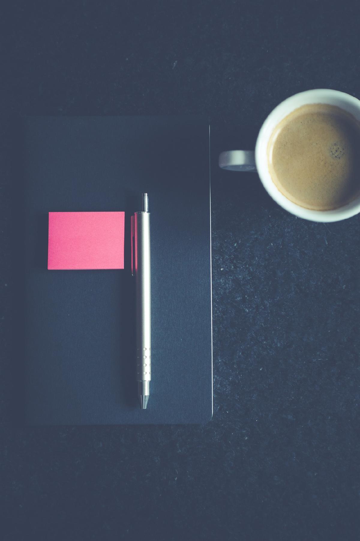 Pen on top of notebook post it notes and mug of coffee