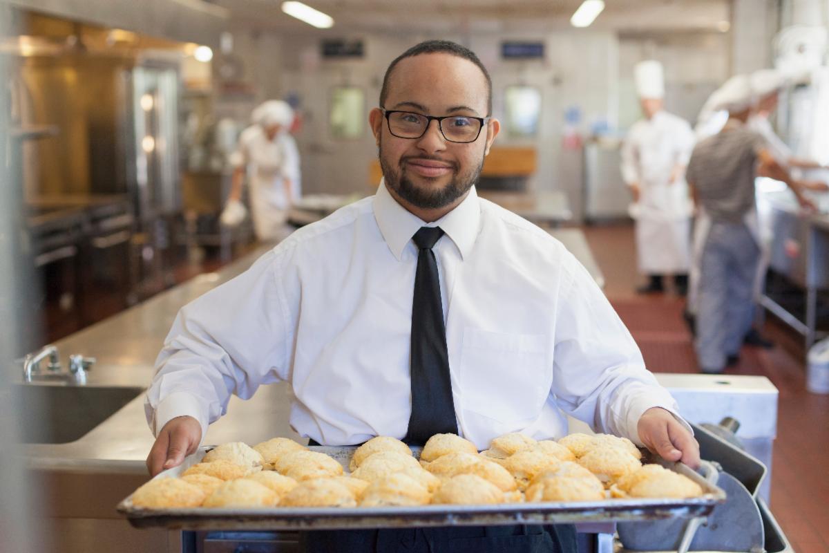 Person with a disability holding a tray of pastries while working at a restaurant