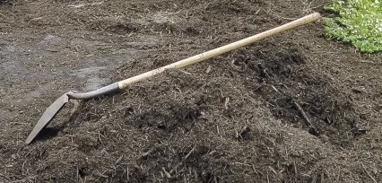 A shovel is leaning against a pile of compost.