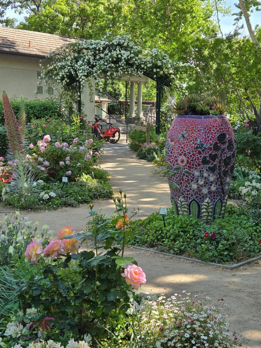 A garden pathway leading to a trellis with abundant garden flowering plants.