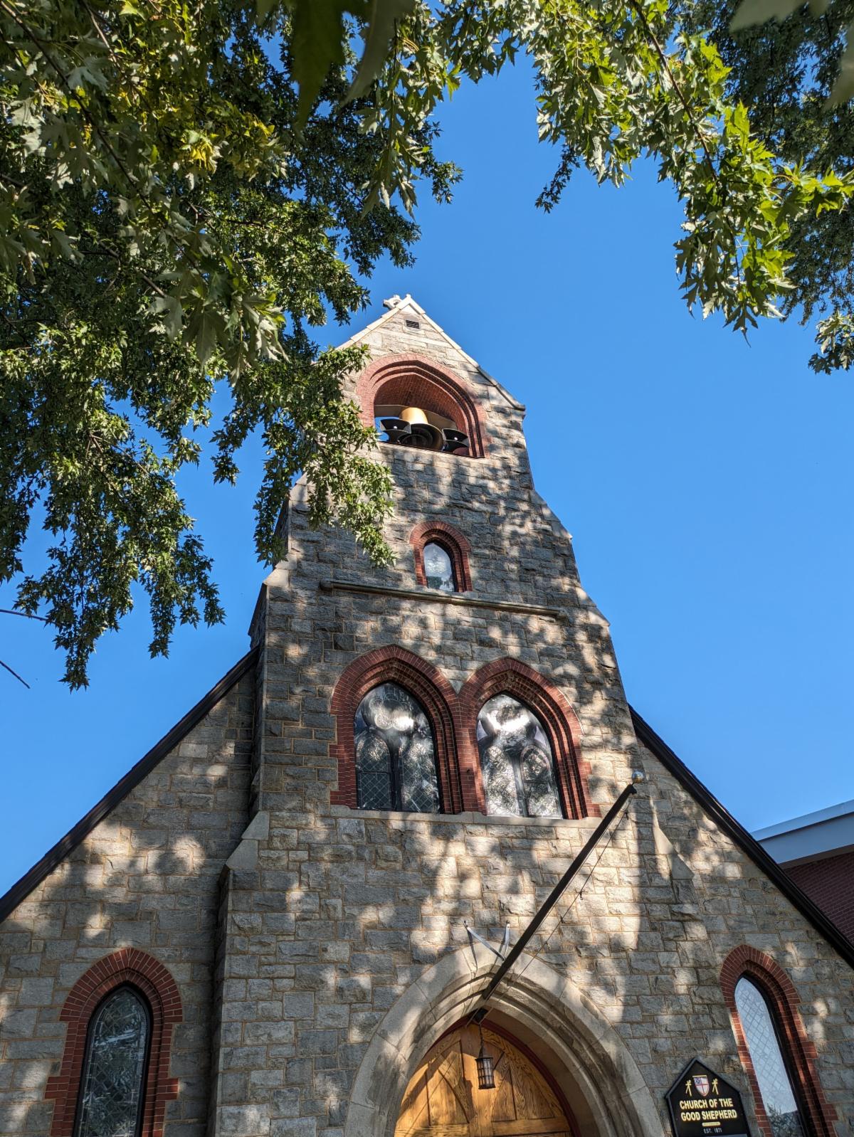 church steeple against a blue sky framed by leaves