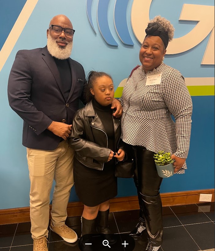 An African American girl with Down syndrome  stands with her parents.