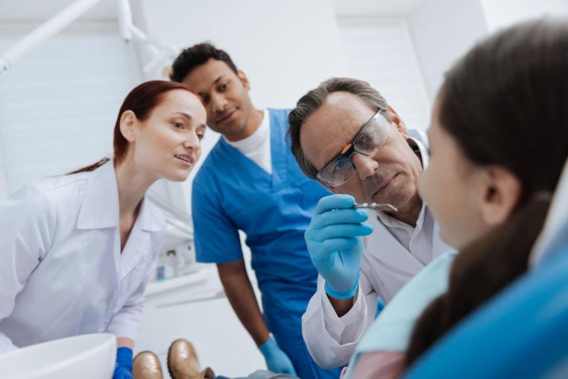 A male and female student both watch on as a dentist examines a young girl's mouth.