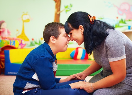 profile of loving mother touching foreheads with her son with a disability, both are smiling