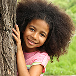 Una ni_a peque_a y t_mida mira desde detr_s de un _rbol.