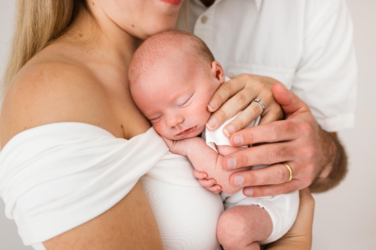 sweet mom and dad caress baby girl close to chest