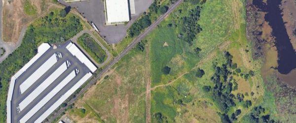 Arial shot of the brownfield site, large gray and white concrete area between green fields